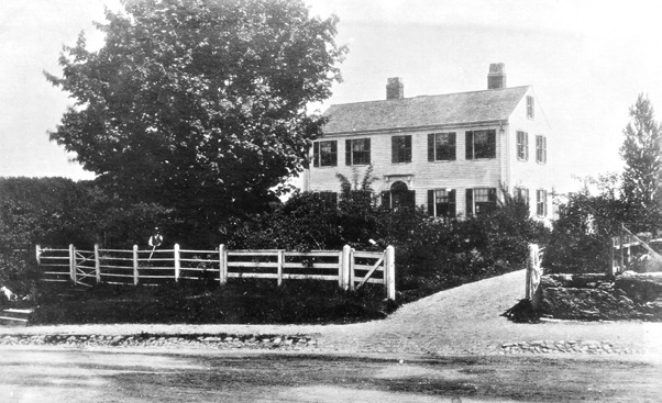 Black-and-white photograph of house with fence and gravel drive