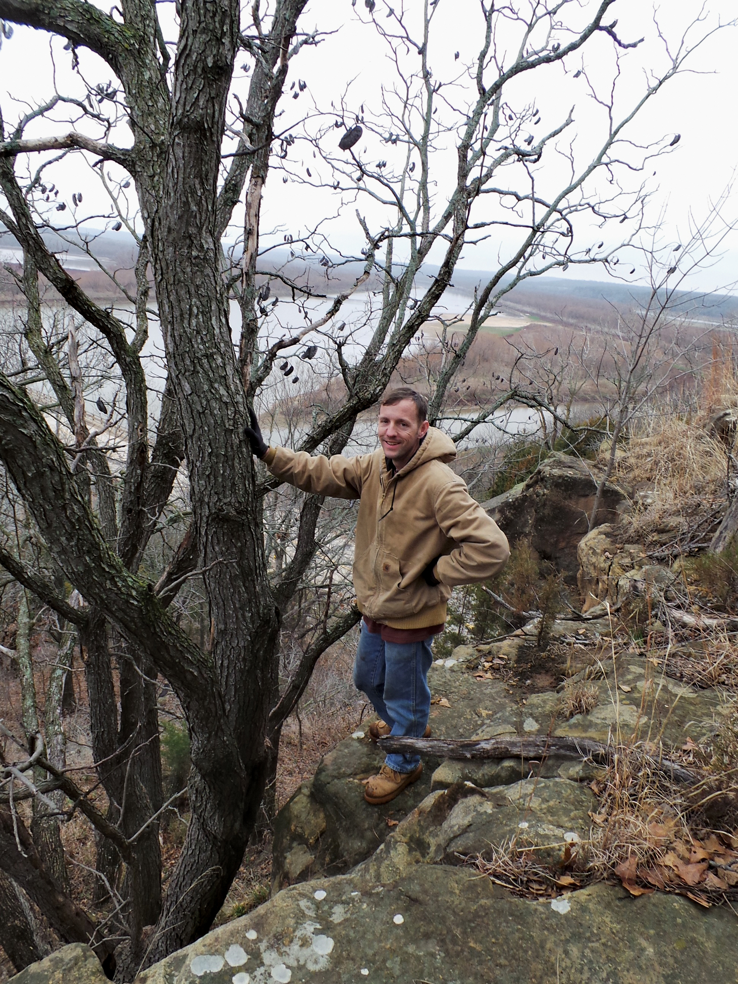 Photo of author standing beside coffeetree with floodplains below