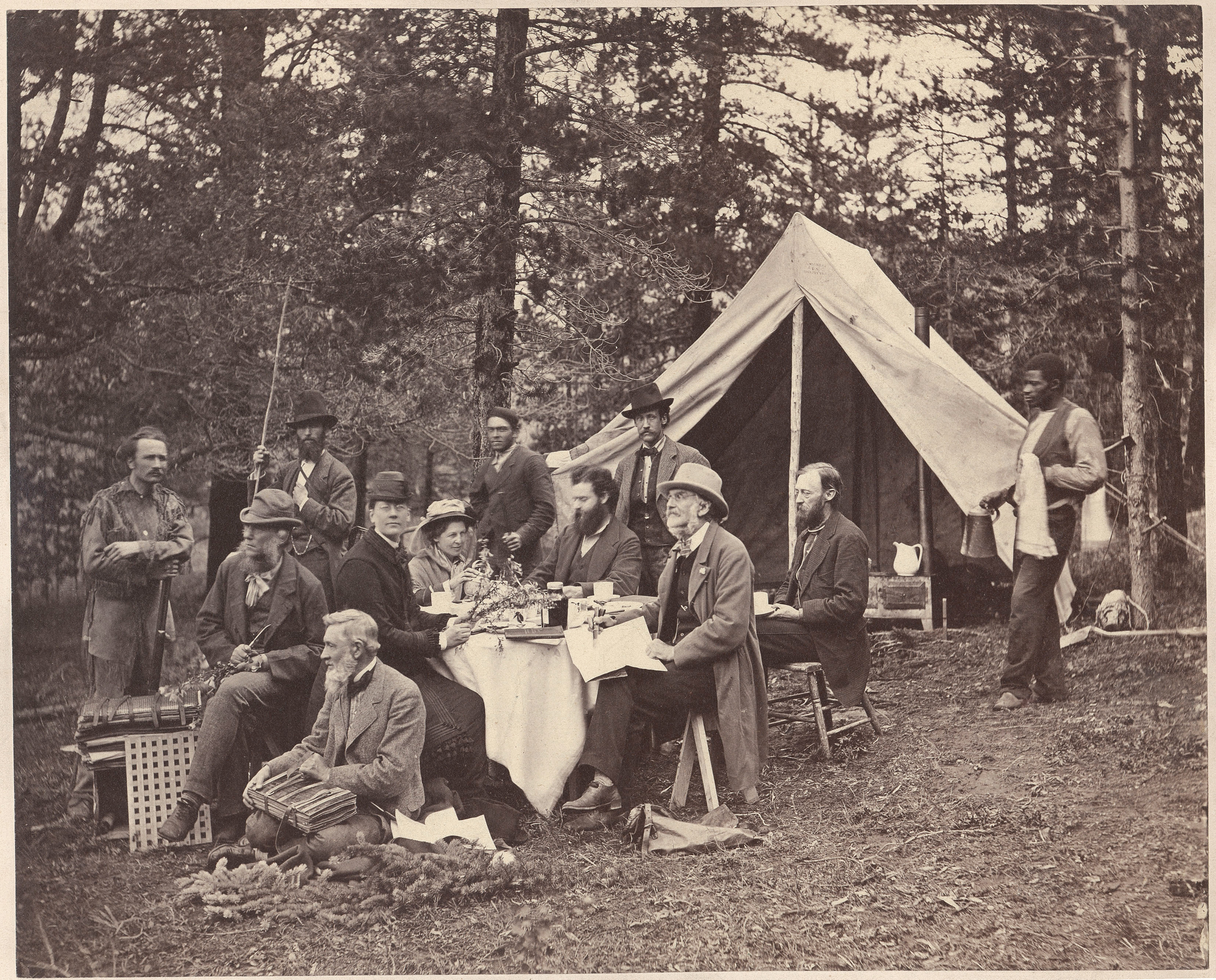 Sepia-colored photo of seated individuals sitting in front of pitched canvas tent