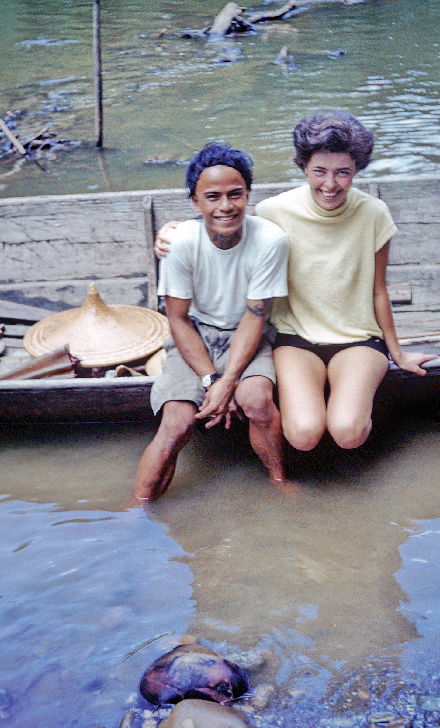 Mary Ashton sitting with Asah on the edge of a boat with feet in river