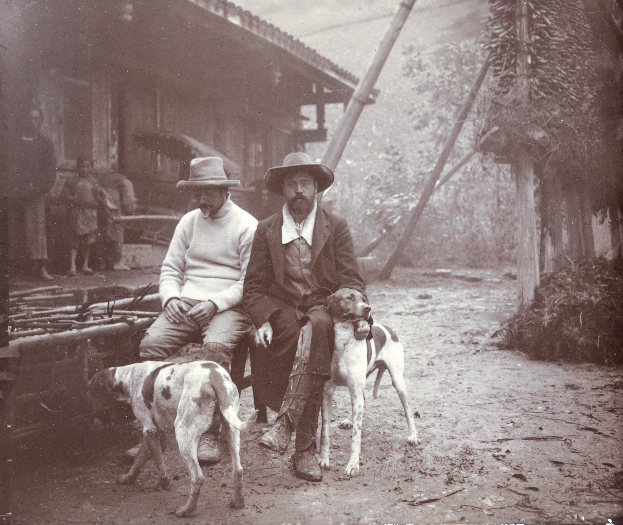 Sepia photo of two men sitting with two dogs