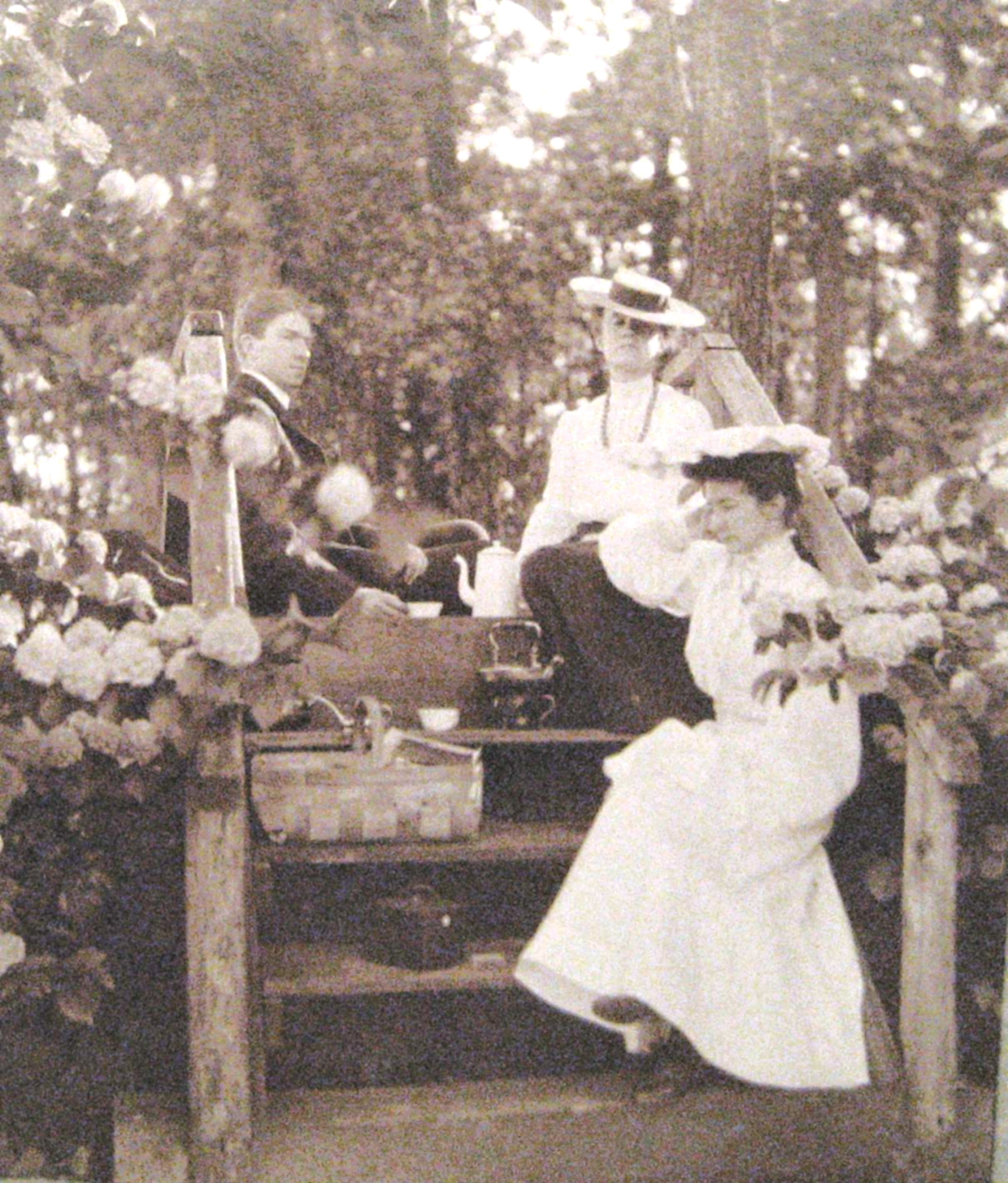 Sepia photograph of three young adults sitting on staircase with picnic items arrayed around them