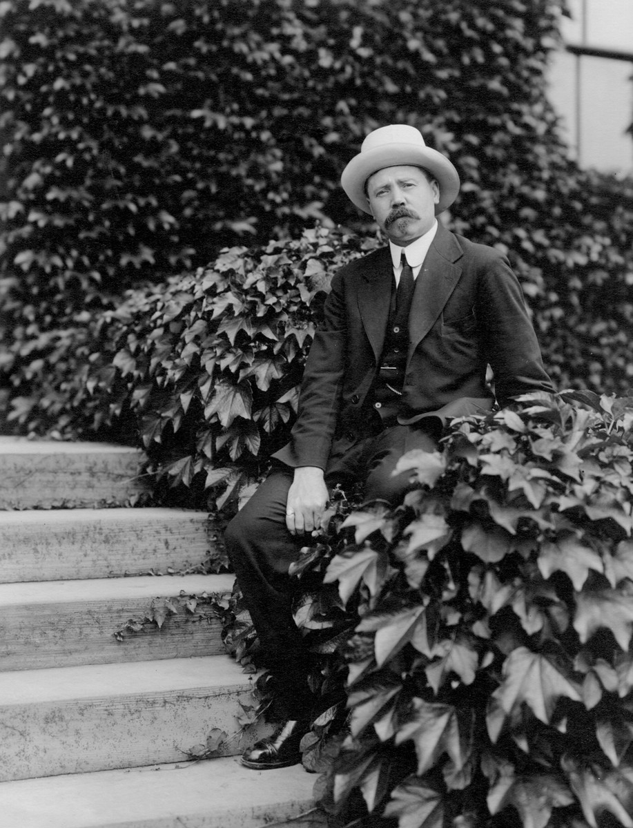 Man sits among ivy on the steps of a large building