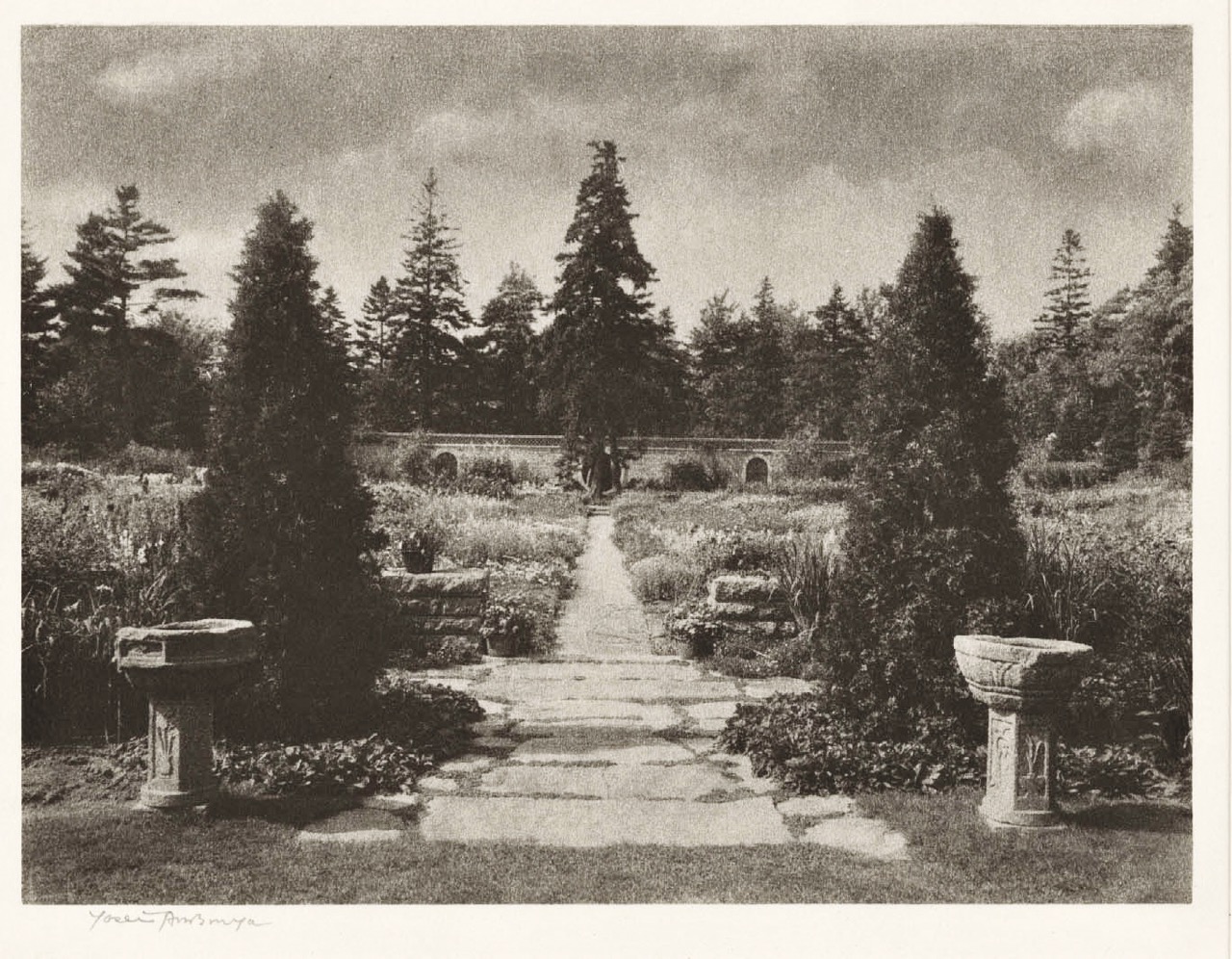 black and white one-point perspective photo of garden with two urns at head of path leading to distant wall.