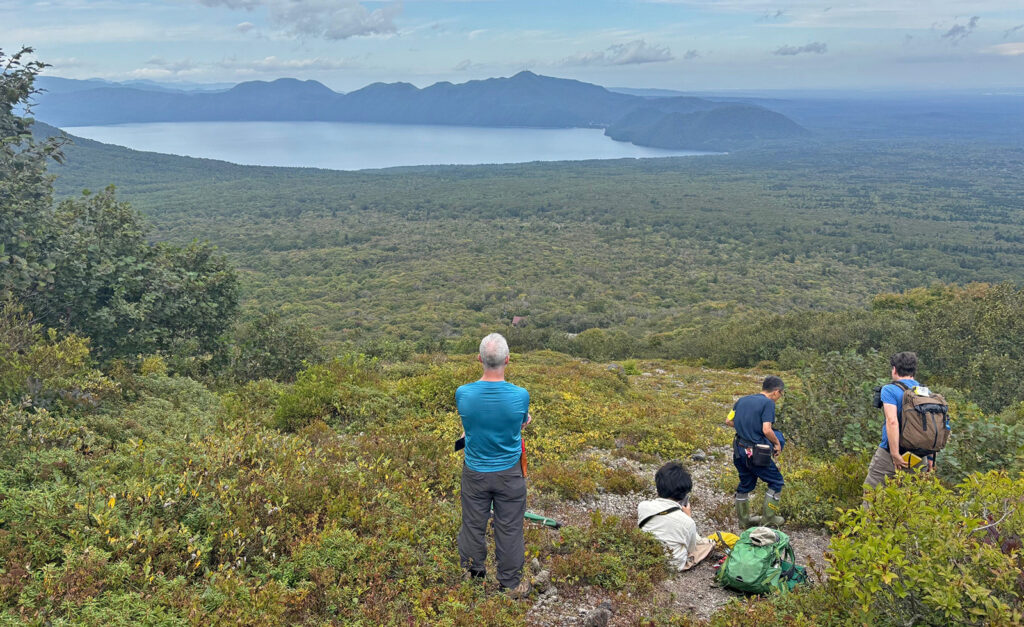 The team takes a break to enjoy the view of Lake Shikotsu after collecting Gaultheria pyroloides, Weigela middendorfiana, and Eubotryoides grayana on the side of Mt. Tarumae in Hokkaido.