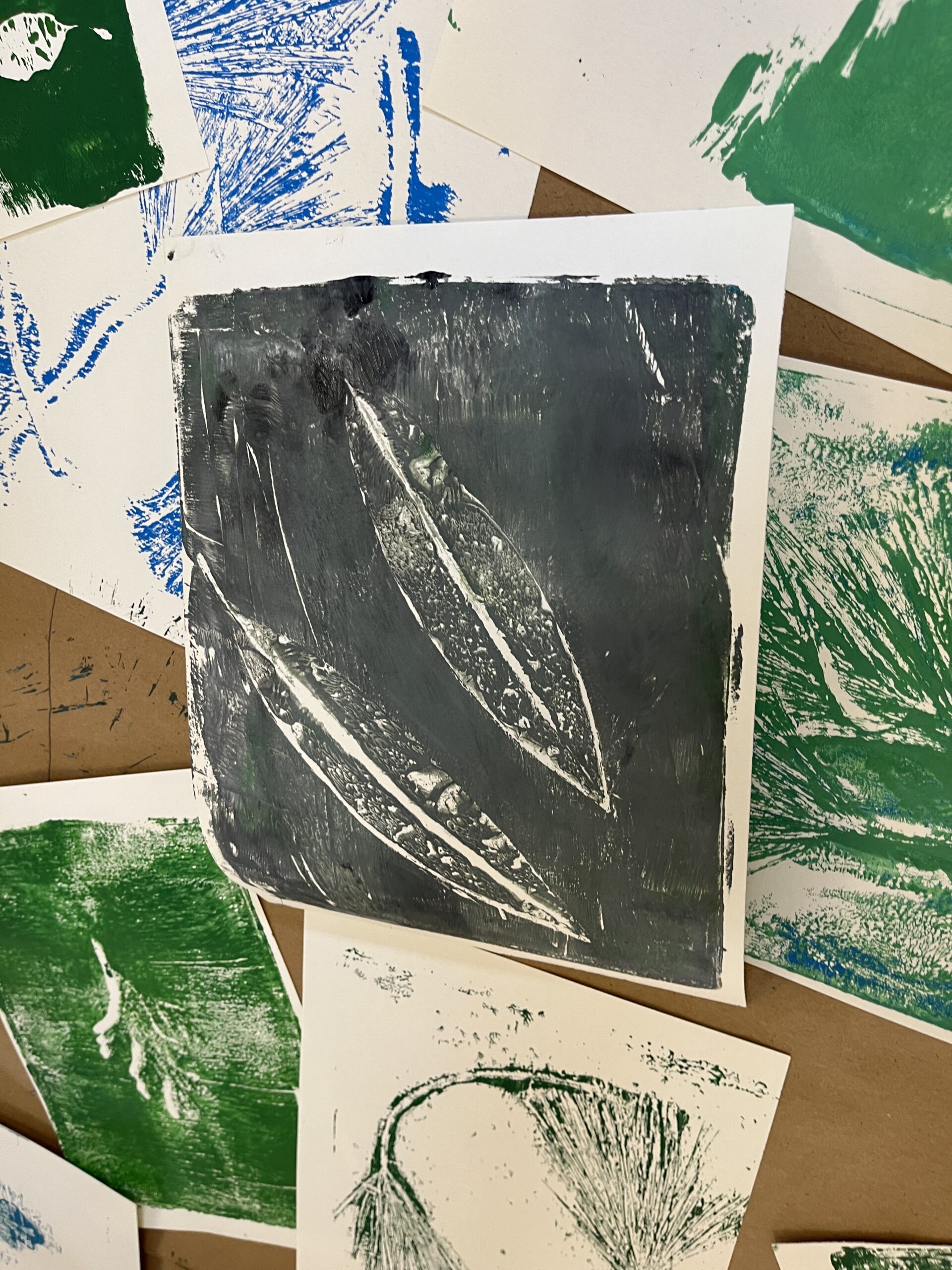 A group of gel prints in the center is a black print of two leaves.