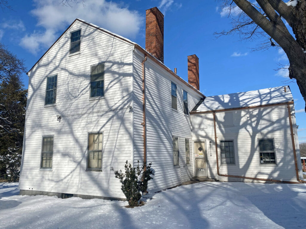 View of a white frame, two story house with an ell in the rear and two chimneys.