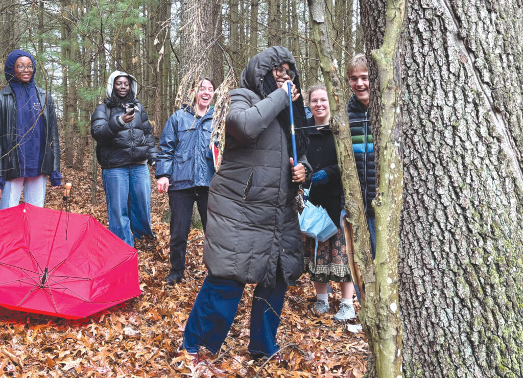 A student holds a coring device on the trunk of an oak tree as several students look on.