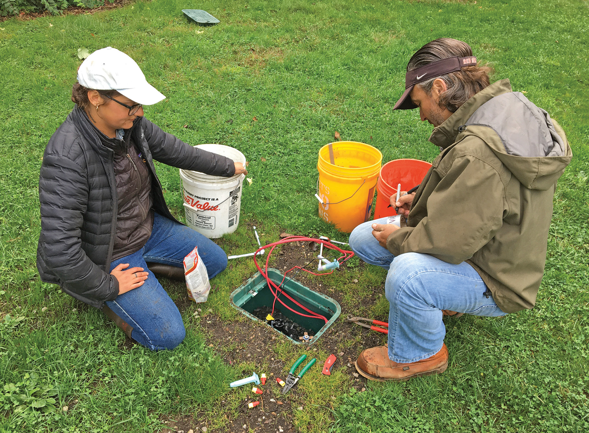 Two people work beside a hole in the ground with wires coming out