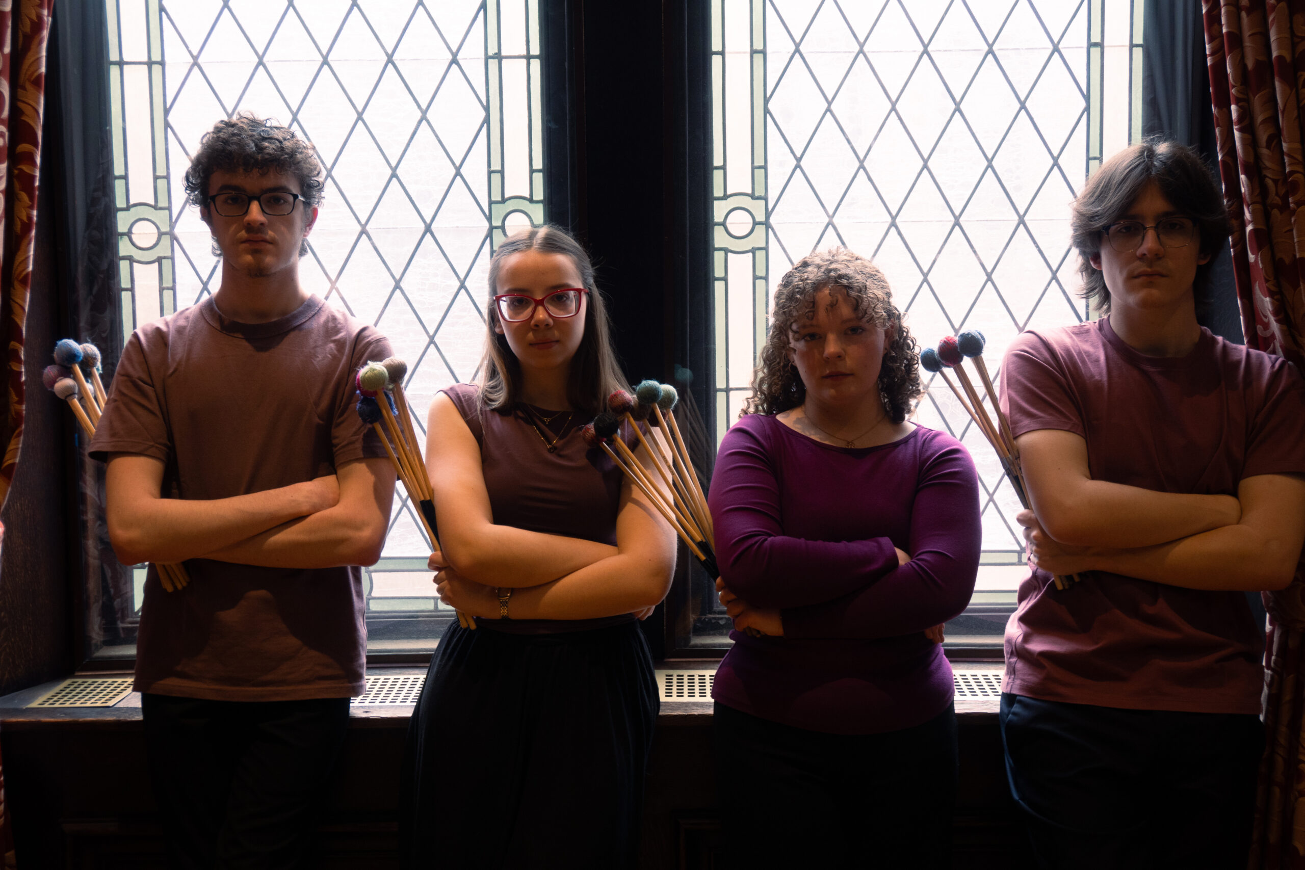 Four people stand side by side, holding percussion mallets