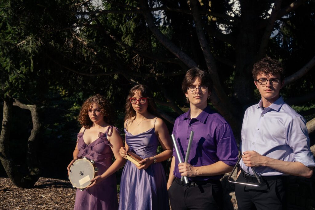 Four people stand in a garden holding percussion instruments